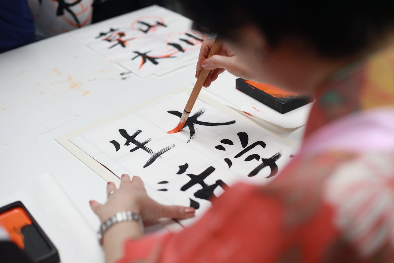 Inicio Close-up of a person practicing traditional Japanese calligraphy with a brush on paper.