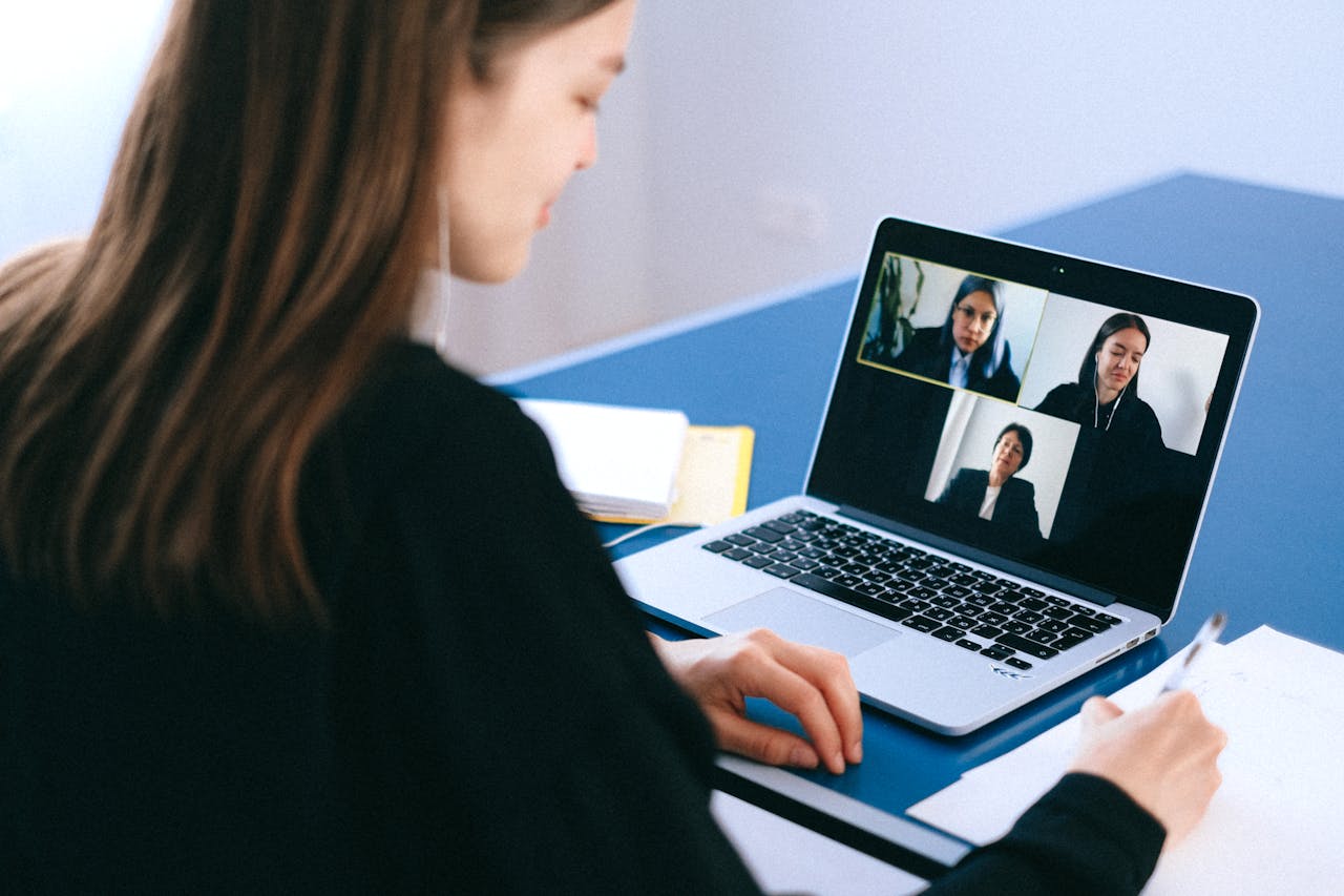 Contact A woman engaging in a video conference using a laptop at home, taking notes.