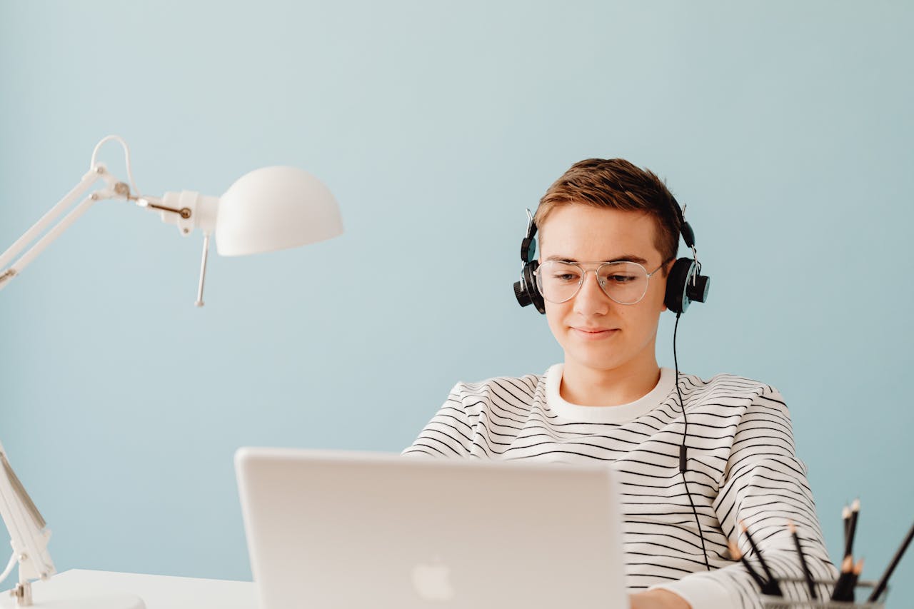 Inicio Teenager with headphones working on laptop in home office, exemplifying remote learning.